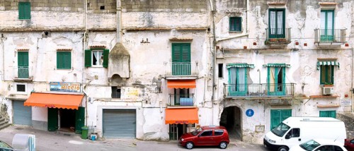 old dilapidated facade of a residential building with balconies and a used car dealer in Minori,