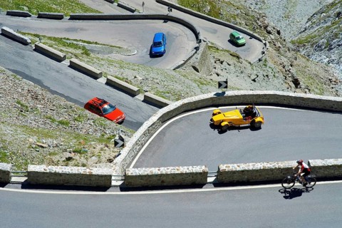 A red, green and blue car, a yellow roadster and a bicycle driver in hairpin curves on the Stelvio