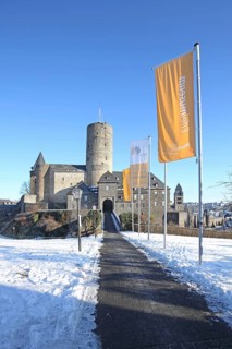 Landmark Genovevaburg built 13th century with keep Goloturm in winter and flags Eifelmuseum, path,