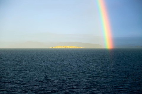 Seascape view of spectrum colours in rainbow over sea and island, Norway, Europe