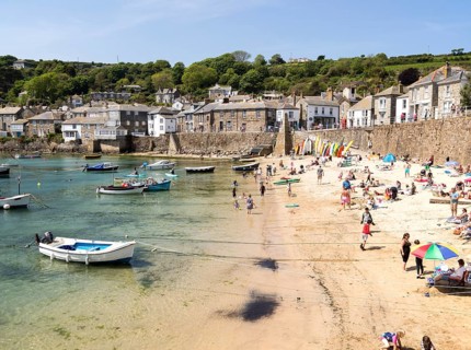 People on crowded beach in Mousehole village, Cornwall, England, UK
