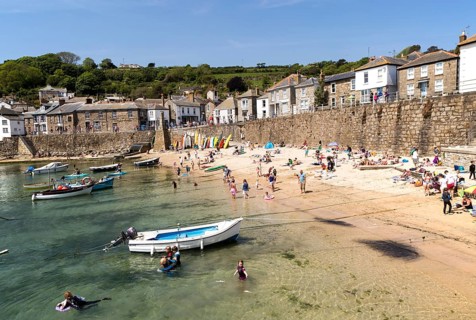 People on crowded beach in Mousehole village, Cornwall, England, UK