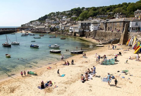 People on crowded beach in Mousehole village, Cornwall, England, UK