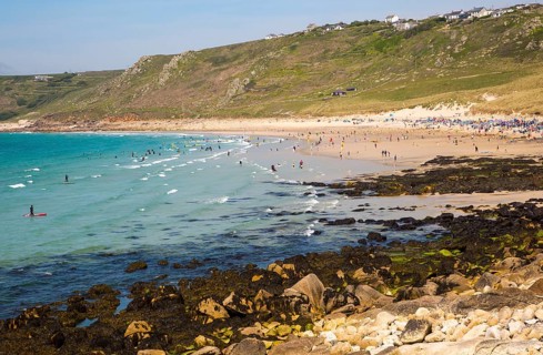 Coastal scenery with busy crowded sandy beach, Sennan Cove, Land's End, Cornwall, England, UK