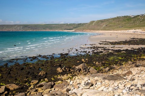 Coastal scenery with busy crowded sandy beach, Sennan Cove, Land's End, Cornwall, England, UK