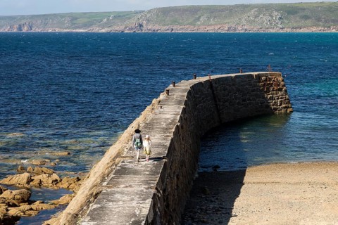 Woman and girl walking on breakwater quay, Sennen Cove, Land's End, Cornwall, England, UK