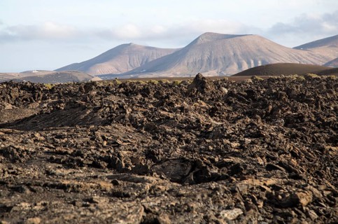 Volcanic landscape of solidified lava flows and distant cone volcanoes, near Yaiza, Lanzarote,