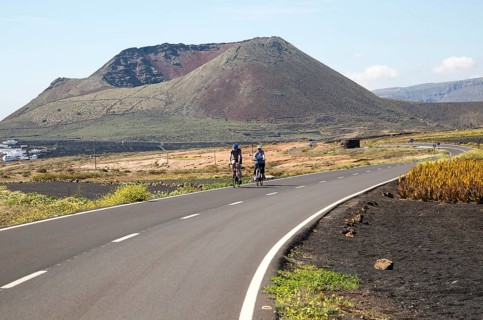 Cyclists on road leading to cone of Mount Corona volcano and Ye village, Haria, Lanzarote, Canary
