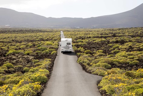Motorhome on straight sealed tarmac road crossing lava flows Malpais de Corona, Lanzarote, Canary