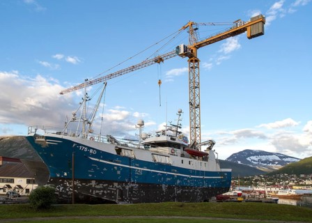 Construction crane towering above fishing boat boat in dry dock, Tromso, Norway, Europe