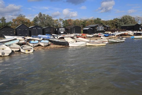Dinghy boats and black wooden fishing sheds, River Ore, Orford, Suffolk, England, UK
