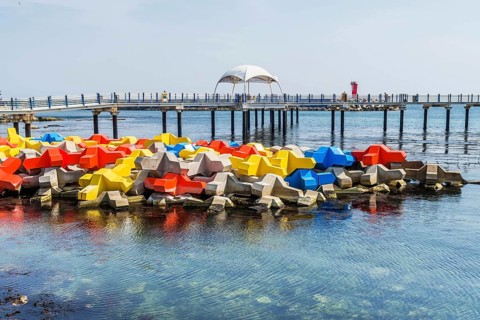 Large blocks of concrete in primary colors in water with boardwalk in background in Goseong, South