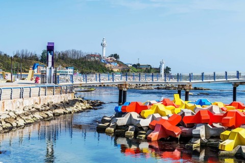 Colorful breakwater blocks in ocean water with lighthouse on hill in background in Goseong, South