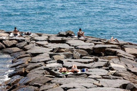 Tourists sunbathe on a stone groyne jutting out into the sea, Imperia, 01.06.2022