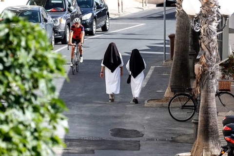 Two nuns walk across a street in Diana Marina, a man on a racing bike rides past, 28/05/2022