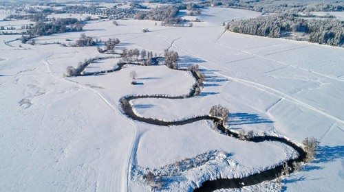 Drone shot of the river Schmutter meandering naturally through the snowy winter landscape of the