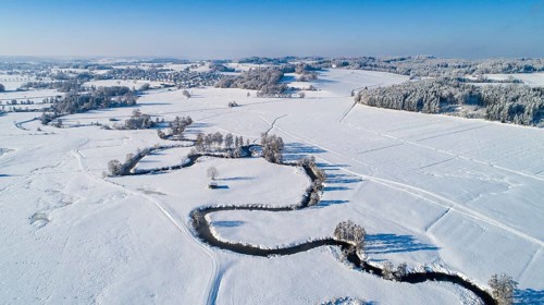 Drone shot of the river Schmutter meandering naturally through the snowy winter landscape of the