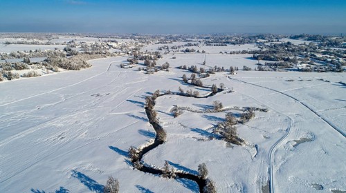 Drone shot of the river Schmutter meandering naturally through the snowy winter landscape of the