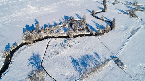 Drone shot of the river Schmutter meandering naturally through the snowy winter landscape of the