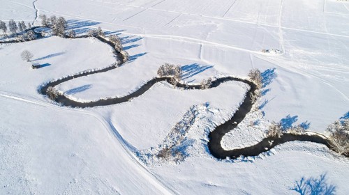 Drone shot of the river Schmutter meandering naturally through the snowy winter landscape of the