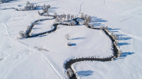 Drone shot of the river Schmutter meandering naturally through the snowy winter landscape of the