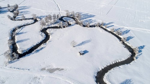 Drone shot of the river Schmutter meandering naturally through the snowy winter landscape of the