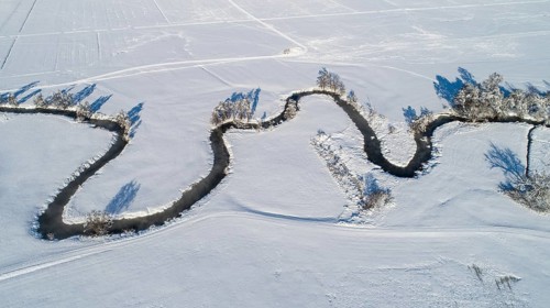 Drone shot of the river Schmutter meandering naturally through the snowy winter landscape of the