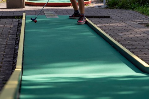 Boy hits ball on green minigolf course