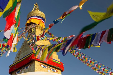 Golden spire of Boudhanath, the Bouddha Stupa, and colourful Buddhist prayer flags. It is the