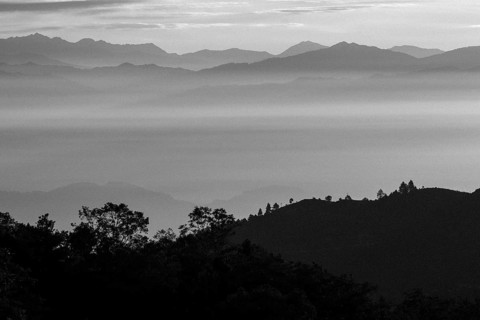 Silhouettes of Himalayan mountain ridges above the clouds in the valleys and some trees in the