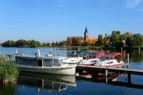 Boats lying on a calm lake in front of a church surrounded by trees under a clear blue sky, ships,