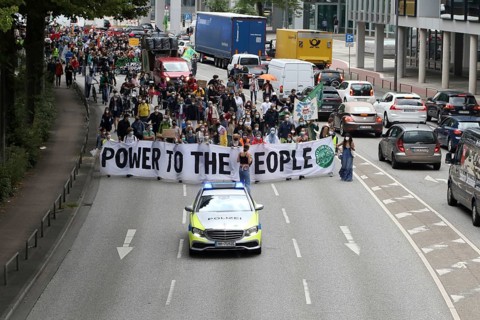 Police car and demonstrators behind banner with the inscription Power to the people at the alliance