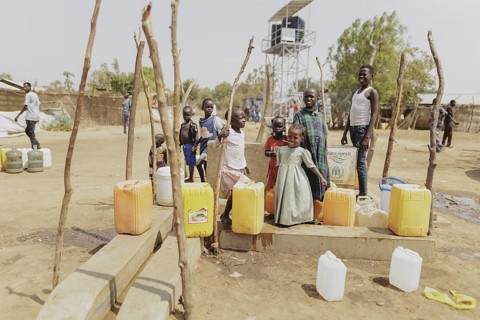 Children and adults stand with water canisters at a well in the Gorom refugee settlement southwest