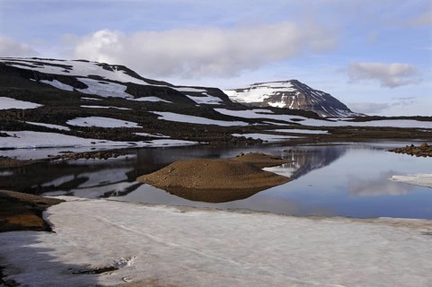 Still partly-frozen meltwater pool and the mountain Bjolfur in the Fjardarheidi range near