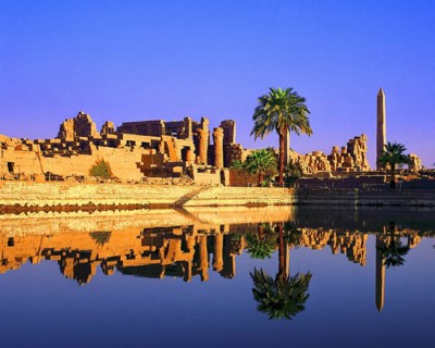 Palm trees grow beside the cistern, obelisk, columns and other remains at temple of Karnak, Luxor,