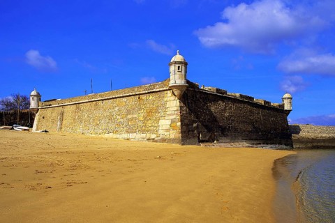 Golden sand on the beach at Lagos, with the old harbour defenses, the 17th century Forte Bandeira,