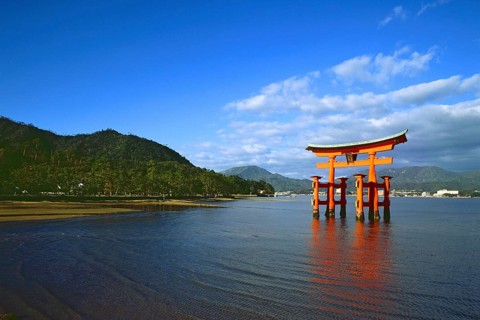 The bright red Sea-gate of Miyajima temple, Japan, against a background of sea and the low hills