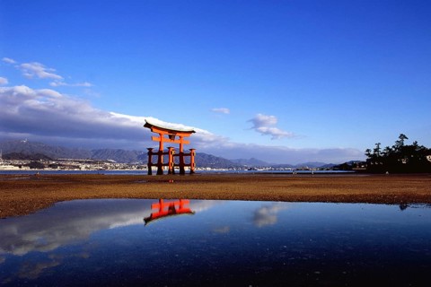 The bright red Sea-gate of Miyajima temple, Japan, against a background of sea and the low hills
