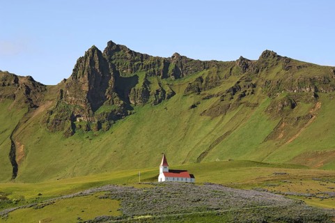 Small red and white church on a hilltop, surrounded by crags and steep hillsides, above the town of