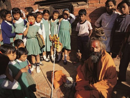 A group of young schoolgirls gathers round fascinated by a Hindu holy man or saddhu outside the