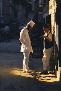 Two men chat in a patch of sunlight in a Kathmandu backstreet, Kathmandu, Nepal, Asia