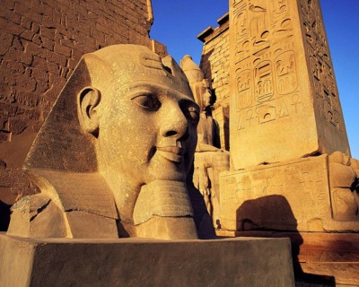 Carved head of King Rameses II in early morning sunlight with inscribed column and other carvings