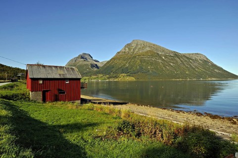 Red wooden boathouse at Lia with the island of Aldra and the Hjarttinden peaks behind, north-west