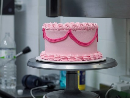 A pink ruffled cake displayed on a rotating stand in a professional kitchen lab of bakery