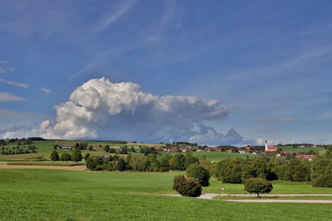 Threatening thundercloud over a sunny, hilly landscape with a village in the foothills of the Alps,