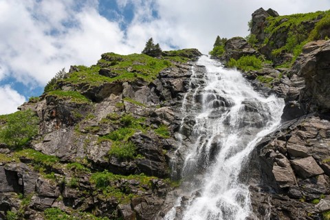 A gushing waterfall cascades over rocky slopes under the blue sky, Capra Waterfall, Goat Waterfall,