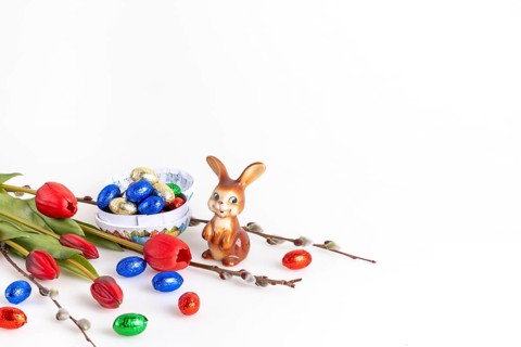 Easter composition with an Easter bunny and a bowl full of chocolate eggs, white background, copy
