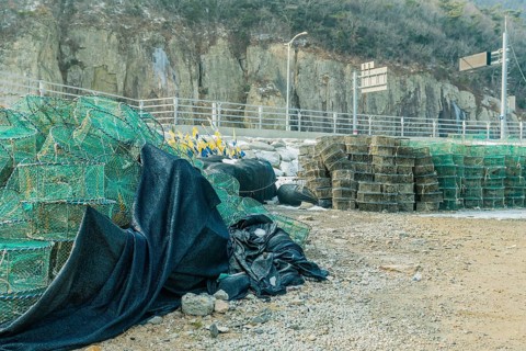 Lobster traps stacked in gravel lot with mountain cliff in background in South Korea