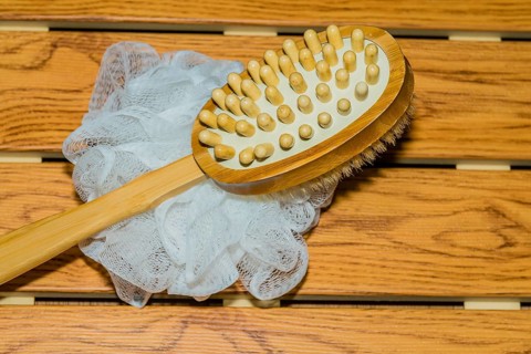Bath and massage brush and white scrubbing pouf bath sponge on wood grain background