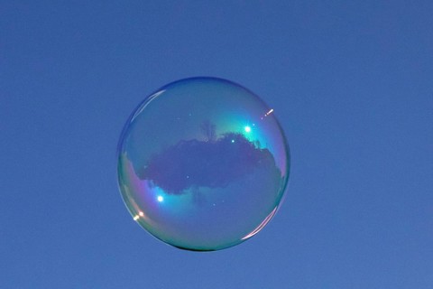 Soap bubbles coloured film of soapy water with reflection in front of blue sky